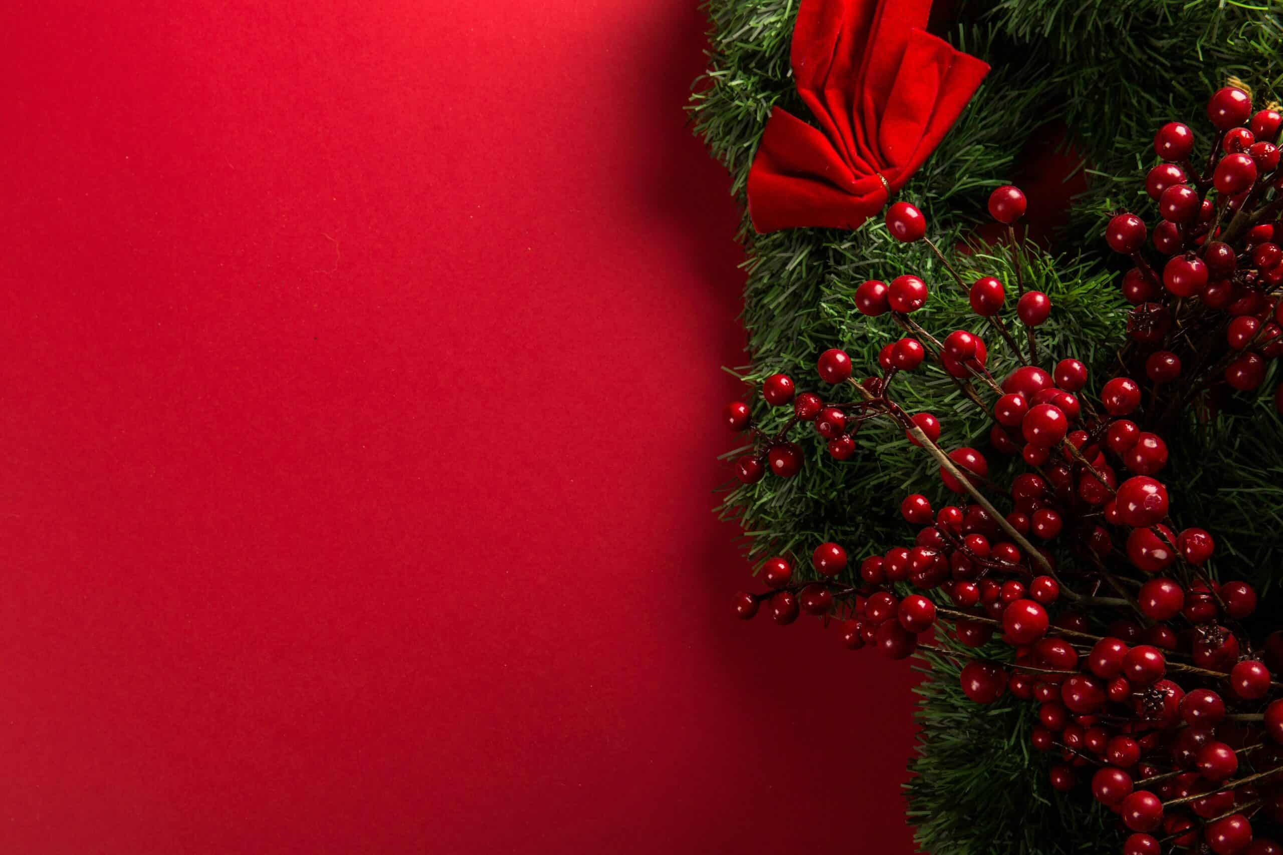 Red Christmas wreath with berries and bow on a vibrant red background.