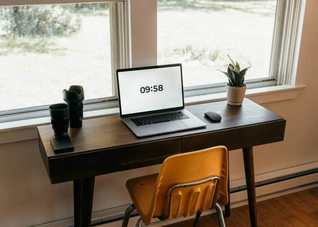 Modern home office desk setup with laptop, camera lenses, and potted plant.