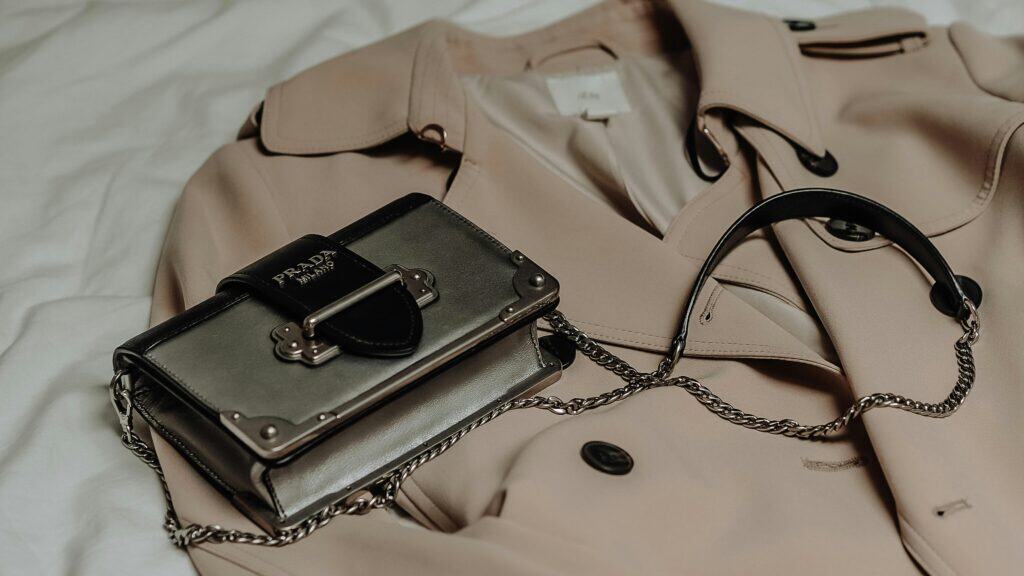 Prada leather cross-body bag with a chain strap resting on a beige trench coat, illustrating a luxury fashion accessory.
