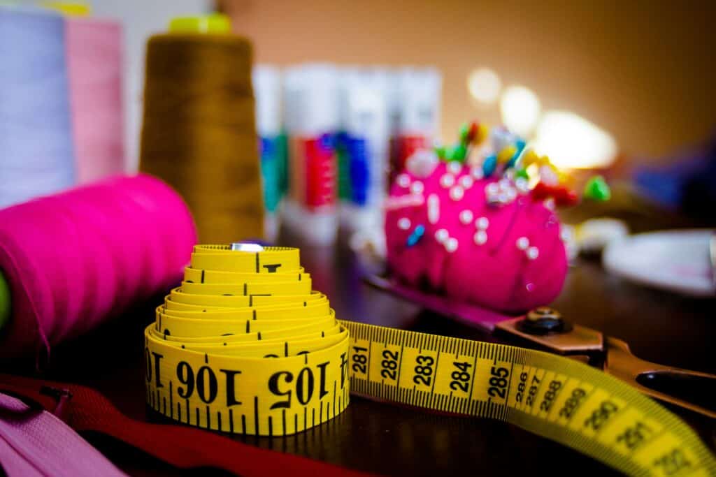 Close-up of a yellow measuring tape, colorful sewing threads, and a pink pincushion with pins on a fashion designer’s workspace.