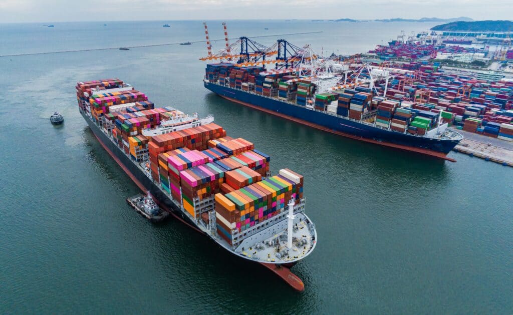 Tariffs Are Reshaping Fashion, But the Brands That Keep Hiring Will Come Out Ahead 3 "Aerial view of cargo container ships at port, representing the global supply chain disruptions from tariffs affecting the fashion industry